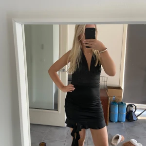 Svart kort klänning - Säljer en snygg svart kort klänning med v-ringning och öppen rygg. Den har en knytning i nacken och en liten slits på sidan. Perfekt för fest eller en utekväll! Klänningen är i bra skick och passar till många olika tillfällen.