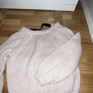 Ljusrosa stickad tröja med svart rosett - Mysig ljusrosa stickad tröja med en söt svart rosett i halsen. Perfekt för kyliga dagar och ger en stilren look. Tröjan har långa ärmar och är superbekväm att ha på sig. Passar perfekt till både vardag och fest!