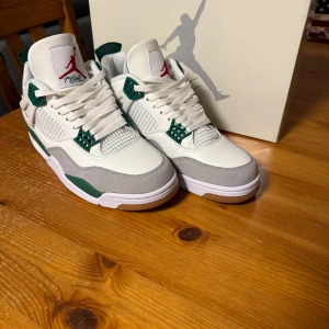 Nike Air Jordan 4 Pinegreen - Säljer ett par snygga Nike Air Jordans i vitt och grönt. Skorna har en cool design med gråa detaljer och klassisk snörning. Perfekta för både vardag och fest! De är i nytt skick och kommer med originalkartong.