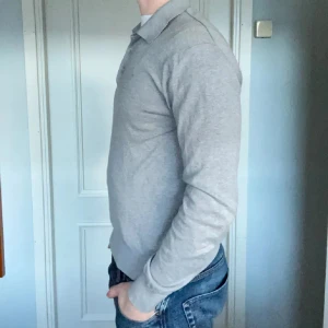 Grå pikétröja - Säljer en stilren grå pikétröja i normal passform. Tröjan har långa ärmar och en klassisk krage med knappar. Perfekt för både vardag och lite mer uppklädda tillfällen. Skön och enkel att matcha med jeans eller chinos.