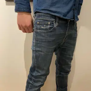 Säljer ett par snygga blå jeans från Jacob Cohën i bra skick. De har en klassisk femficksdesign med knappgylf och märkeslogga på insidan av midjan. Jeansen har en slim passform. De är tillverkade i högkvalitativt denim. De har en liten skada på vänstra knät men annars väldigt bra skick. Säljer då de inte kommer till användning och har blivit för små! 