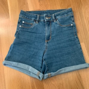 Blå jeansshorts från Cubus - Säljer ett par snygga blå jeansshorts från Cubus i storlek XS. De är högmidjade med klassisk femficksdesign och har en bekväm passform. Perfekta för sommardagar eller en avslappnad vårlook. Shortsen har en snygg uppvikt kant som ger en extra touch av stil.