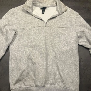 Grå halvzip tröja från H&M - Säljer en stilren grå halvzip tröja från H&M. Perfekt för både vardag och avslappnade tillfällen. Tröjan har en dragkedja vid halsen och är tillverkad i mjukt material för extra komfort. Passar bra till jeans eller joggers! Köptes för 400:-