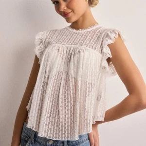 Vit spetsblus från Nelly - Säljer en superfin vit spetsblus från Nelly i storlek XS. Blusen har korta ärmar med volangdetaljer och en söt knytning i ryggen. Perfekt för sommaren eller en festlig tillställning. Den är gjord av ett lätt och luftigt material som känns skönt mot huden.