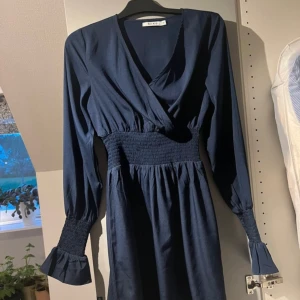 Mörkblå långärmad klänning från NA-KD - Säljer en superfin mörkblå klänning från NA-KD. Den har långa ärmar med smockdetaljer vid ärmsluten och en v-ringad omlottdesign. Perfekt för både vardag och fest! 💙