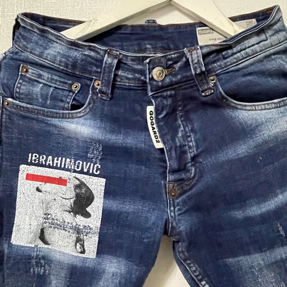 Säljer ett par mörkblå jeans med coolt Ibrahimovic-tryck på framsidan. Jeansen har en slitna detaljer och en knappgylf. De är i bra skick och perfekta för en avslappnad stil. Passar både till vardags och fest!. Jeans & Byxor.