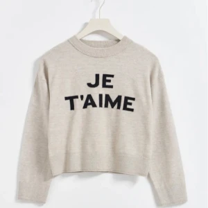 Beige stickad tröja med text - Säljer en superfin beige stickad tröja med texten 'JE T'AIME' i svart på framsidan. Tröjan är croppad och har långa ärmar. Perfekt för höst och vinter! 🧡