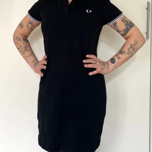 Fred Perry t-shirtklänning - Supersnygg miniklänning från Fred Perry. Avslappnad och skön men med ett stilat intryck. Styla den sportigt, preppy eller punkigt, den funkar i alla lägen!  Använd fåtal ggr och är som ny. 