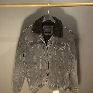 Grå jeansjacka från Zara - Säljer en snygg grå jeansjacka från Zara med en mysig svart fuskpälsfoder. Jackan har långa ärmar och knappar framtill. Perfekt för höst och vår!
