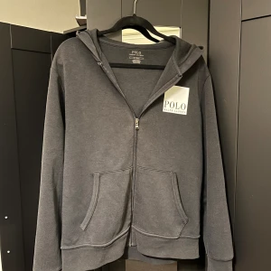 Mörkgrå hoodie från Polo Ralph Lauren - Säljer en snygg och bekväm Svart hoodie från Polo Ralph Lauren. Den har en dragkedja framtill och en stor logga på både bröstet och ryggen. Perfekt för en avslappnad stil och passar till alla tillfällen. Den har långa ärmar och en skön huva. Passar S och M