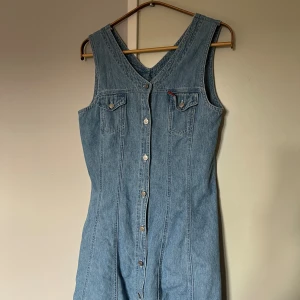 Klänning i jeanstyg - En jättefin, kortare jeansklänning som är lite insydd i midjan för en mer figursydd passform. Knapparna är hur coola som helst med små planeter på, köpt second hand och har ett litet hål i nedre kanten. Passar nog M/L bäst, köpare står för frakt.💛
