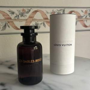 Säljer en elegant och lyxig parfymflaska från Louis Vuitton, Les Sables Roses. Doften har nyckelnoter av Centifolia-ros, bulgarisk rosessens, oudträ, ambra, svartpeppar och saffran. Perfekt för den som älskar en djup och blommig doft med en kryddig twist. I princip oanvänd. 100 ml