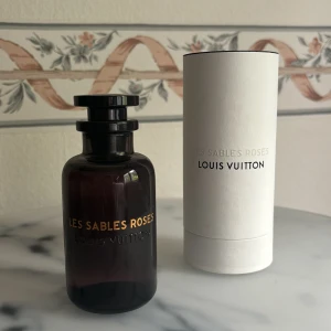 Les Sables Roses Parfym från Louis Vuitton - Säljer en elegant och lyxig parfymflaska från Louis Vuitton, Les Sables Roses. Doften har nyckelnoter av Centifolia-ros, bulgarisk rosessens, oudträ, ambra, svartpeppar och saffran. Perfekt för den som älskar en djup och blommig doft med en kryddig twist. I princip oanvänd. 100 ml