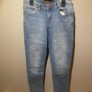 Ljusblå jeans från Jack & Jones - Snygga ljusblå jeans från Jack & Jones med klassisk femficksdesign och knappgylf. Perfekta för en avslappnad stil. Märkesdetaljer på baksidan och slitna effekter för en trendig look.