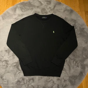 Svart tröja från Polo Ralph Lauren - Säljer en snygg svart tröja från Polo Ralph Lauren med det klassiska gröna logotypbroderiet på bröstet. Tröjan har långa ärmar och en rund halsringning. Perfekt för en avslappnad och snygg look.