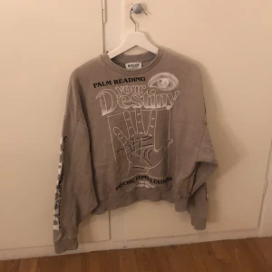 Beige sweatshirt från Madlady - Säljer en beige sweatshirt från Madlady med tryck på framsidan som säger 'Palm Reading Your Destiny'. Tröjan har långa ärmar och en avslappnad passform. Perfekt för en chill dag.
