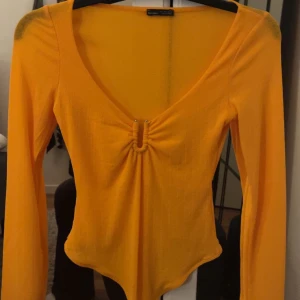 Gul långärmad body  - Snygg gul långärmad body från bershka  med v-ringning och rynkdetalj framtill. Fint skick, endast använd en gång 