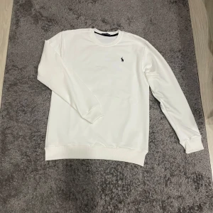 Vit tröja från Ralph Lauren - Säljer en stilren vit tröja från Ralph Lauren med det klassiska broderade logotypen på bröstet. Tröjan har långa ärmar och en rund halsringning. Perfekt för en avslappnad och snygg look. Vid minsta fundering kontakta oss✔️