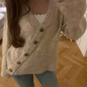 Beige ribbad kofta med knappar - Mysig beige kofta med ribbad struktur och stora knappar framtill. Perfekt för kyliga dagar med sin avslappnade passform och långa ärmar. En stilren och bekväm tröja för alla tillfällen. Nyskick och nästan aldrig använd. Väldigt populär men har tyvärr inte kommit till användning💕💕