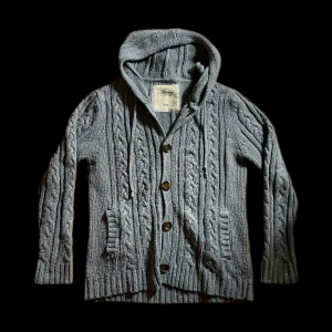 Stickad kofta med luva - Säljer en mysig grå stickad kofta i mycket gott skick med luva och knappar framtill. Koftan har ett snyggt flätmönster och ribbade muddar. Storleken är XXL men den sitter mer som en L. Fråga om mått vid osäkerhet. Perfekt för kyliga dagar! Tveka  inte på att höra av er!