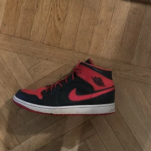 Nike Air Jordans i svart och rött - Snygga Nike Air Jordans i svart och rött med klassisk design. Skorna har en hög modell med snörning och den ikoniska Nike-loggan på sidan. Perfekta för dig som vill ha en stilren och sportig look.