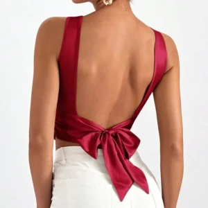 Röd ärmlös topp med öppen rygg och rosett - Snygg röd ärmlös topp med en elegant öppen rygg och en stor rosett. Perfekt för en kväll ute eller en fest. Toppen har en tight passform och är tillverkad i ett glansigt material.