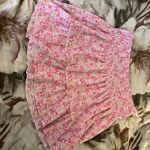 Blommig kjol från Gina Tricot - Söt blommig kjol från Gina Tricot i rosa och grönt. Kjolen har en volangdetalj och är kort med en elastisk midja så den passar både L/XL💞 säljer för att den varit lite för stor för mig! Skriv om frågor finns💞pris går att diskutera vid snabb affär!