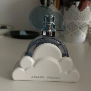 Parfym Ariana Grande Cloud - Säljer en parfym från Ariana Grande med en unik design. Flaskan är blå och formad som ett moln, med en vit molnbas. Perfekt för den som älskar en söt doft. Säljer då jag inte tycker att doften passar mig. Aldrig använd. Parfym och parfymhållare ingår, originalförpackning ingår ej. Nypris 525kr, villig att sänka priset om rätt pris föreslås.