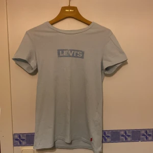 Ljusblå t-shirt från Levi's - Säljer en ljusblå t-shirt från Levi's med deras klassiska logga tryckt på bröstet. T-shirten är kortärmad och har en rund halsringning. Perfekt för en avslappnad stil.