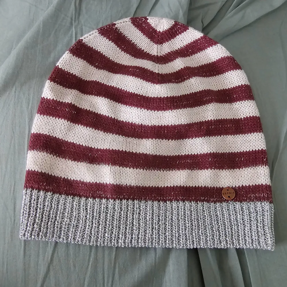 Snygg randig mössa från Esprit i vinrött och vitt med en silver ribbad kant. Perfekt för kyliga dagar med sin stickade design. Mössan har en liten logotypdetalj i metall.. Asusteet.