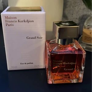 Maison Francis Kurkdjian Grand Soir Eau de Parfum - Elegant och lyxig parfym i en stilren glasflaska med gyllene vätska och en fyrkantig metallkork. Förpackningen är vit med guldtext. Perfekt för den som söker en sofistikerad doftupplevelse.
