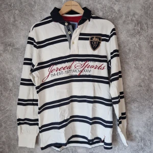 Randig pikétröja från Ciritte - Säljer en stilren randig pikétröja från Ciritte i svart och vit bomull. Tröjan har långa ärmar och en klassisk krage med knappar. Perfekt för en avslappnad och sportig look.