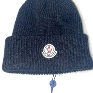 Moncler mössa - Snygg svart ribbad mössa från Moncler med det klassiska logotypmärket framtill. Perfekt för kyliga dagar och ger en stilren look.