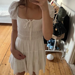 Vit klänning - Charmig vit klänning från Shein med puffiga kortärmar och knytning framtill. Den har en smockad överdel och volangdetaljer i kjolen, vilket ger en romantisk känsla. Storlek: XS