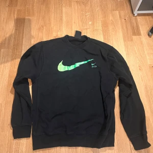 Svart tröja från Nike - Säljer en svart tröja från Nike med en grön logga på bröstet. Tröjan har långa ärmar och en klassisk rund halsringning. Perfekt för en avslappnad stil.