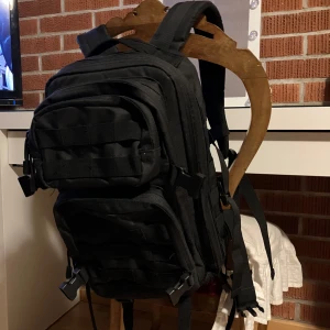 Svart ryggsäck/ frilufts ryggsäck med flera fack - Säljer en svart ryggsäck med flera praktiska fack och justerbara remmar. Den rymmer 30 liter. 2 stora fack, ett mellan och ett litet. Med fler fack och annat i och på! Använd fåtal gånger. Från EMP.