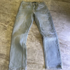 Ljusblå jeans från Scotch & Soda - Säljer ett par ljusblå/ljusgrå jeans från Scotch & Soda. De har en klassisk femficksdesign och en straight passform. Jeansen har slitna detaljer och en läderpatch med logotyp på baksidan.skick 10/10