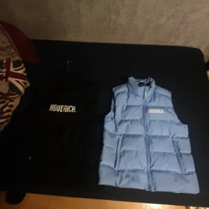 Blå och svart dunväst från Hoodrich - Säljer en snygg blå och en svart dunväst från Hoodrich med dragkedja och logga på bröstet. Perfekt för kyligare dagar när du vill hålla stilen. Västen har en hög krage och är quiltad för extra värme. Jätte bra kvalité! Knappt använd och gör sitt jobb genom att hålla dig varm. Storlek XL och L. Priset Kan diskuteras 😊