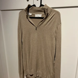 Beige tröja från Selected Homme - Säljer en stilren beige tröja från Selected Homme. Tröjan har en dragkedja vid halsen och långa ärmar. Perfekt för en avslappnad och snygg look.