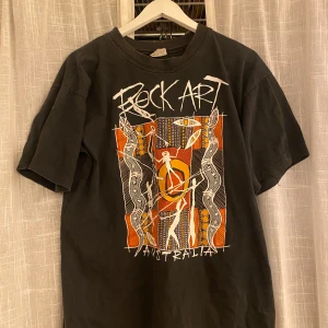 Svart t-shirt med Rock Art Australia-tryck - Cool svart t-shirt med ett färgglatt Rock Art Australia-tryck i orange, vitt och gult. 