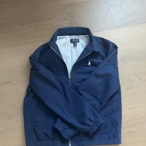 Blå jacka från Polo Ralph Lauren - Säljer en stilren blå jacka från ralph louren, jackan har inga defekter,hål eller någon typ av defekt. storleken är L i ungdom alltså 14-16. Nypris ligger runt 2900. Skriv gärna för funderingar prisförslag och frågor. Mvh Liam🙌🏽