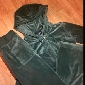 Grön velour hoodie från Juicy Couture - Säljer en snygg grön velour hoodie från Juicy Couture. Den har en dragkedja framtill och en klassisk huva. Perfekt för en avslappnad och stilren look.