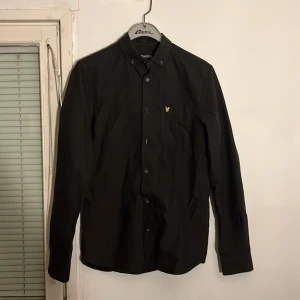 Brun skjorta från Lyle & Scott - Snygg brun skjorta från Lyle & Scott med klassisk design och gul broderad logga på bröstet. Skjortan har långa ärmar och knappar framtill. Perfekt för en stilren look. Storlek Xs/S. Hör av dig om du har frågor.😁