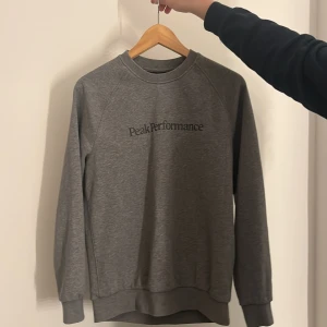 Grå sweatshirt från Peak Performance - Säljer en stilren grå sweatshirt från Peak Performance. Tröjan har en klassisk rund halsringning och långa ärmar. Perfekt för en avslappnad look. Tröjan är använd med är fortfarande i fint skick! Pris kan diskuteras!