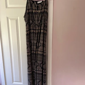 Mönstrad långklänning - Snygg långklänning med geometriskt mönster i svart och beige. Klänningen är ärmlös och har en bekväm passform med resår i midjan. Perfekt för en avslappnad stil.
