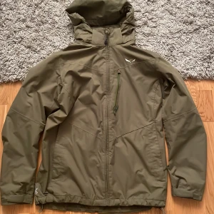 Vindjacka från Salewa - Säljer en olivgrön vindjacka från Salewa med huva och ventilationsmöjligheter för armhålorna. Den är i väldigt bra skick och har inga skavanker över huvud taget. Funkar utmärkt som lätt jacka på våren men även i lite kallare väder då den kan användas som skaljacka. Det står storlek L men upplever att den snarare sitter som M 