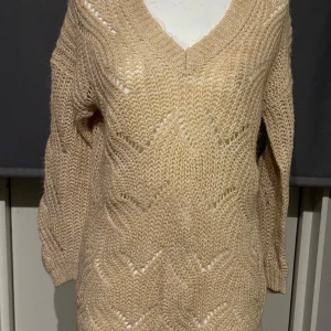 Beige stickad tröja från ONLY - Mysig beige stickad tröja från ONLY med v-ringning och ett snyggt stickat mönster. Perfekt för kyliga dagar med långa ärmar och en avslappnad passform. 