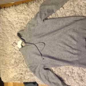 Grå hoodie - Mysig grå hoodie med långa ärmar och en praktisk huva. Perfekt för kyliga dagar och avslappnade stunder. Enkel design som passar till det mesta. Sparsamt använd 