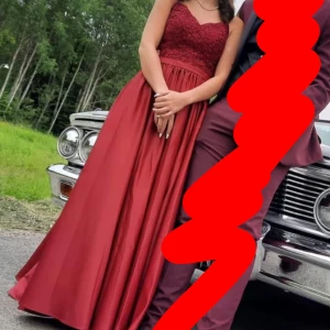 Vinröd balklänning med spetsdetaljer -  Vinröd  balklänning med spetsdetaljer på överdelen.  Klänningen har ett litet släp därbak och en slits men inget som direkt märkes. Använd 1 gång. Storlek oklart om de e xxs eller xs köpt för 1600