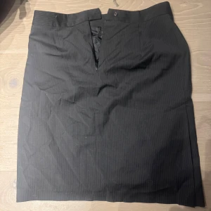Svart kjol från Tiger of Sweden - Elegant svart kjol från Tiger of Sweden med diskreta ränder. Kjolen har en klassisk design med dragkedja fram och är perfekt för en stilren look.